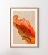 Framed abstract art print featuring a flowing, textured orange and red brushstroke on a warm beige background, housed in a light natural wood frame with a white mat, mounted on a neutral light gray wall.